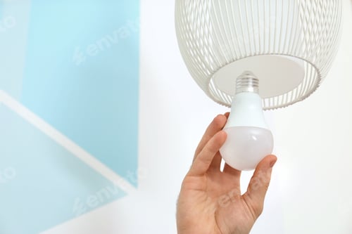 Preview: Man changing light bulb in lamp against color wall, closeup. Space for text
