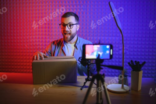 Preview: Joyful young man recording unboxing video in studio