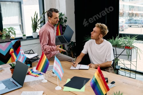 Preview: Two stylish men discussing creative ideas in a vibrant office adorned with pride flags