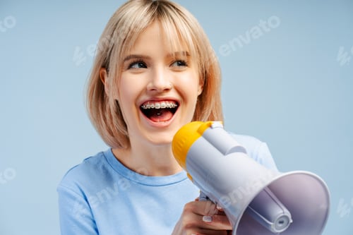 Preview: Attractive young woman with braces and piercing looking away holding and talking into megaphone