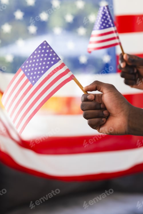 Preview: Two hands wave small American flags against a blurred background