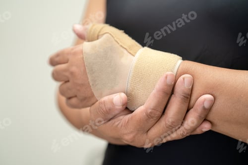 Preview: Asian middle-aged lady woman use elastic bandage to treating De Quervain syndrome at hand and finger