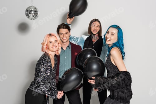 Preview: pleased queer people with black festive balloons smiling at camera on grey background