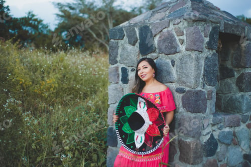 Preview: Mexican woman wearing traditional hat and dress. Outdoor portrait next to stone wall.