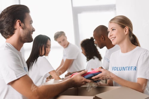 Preview: young volunteers packing clothes for charity with colleagues on background