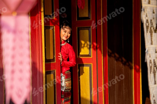 Preview: Young Asian woman wear Thai Lanna dress stand in red color and old style door also look to right