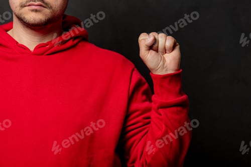 Preview: White guy in red sweatshirt show fist gesture on dark background