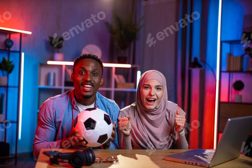 Preview: Mixed race couple emotionally watching soccer game on laptop