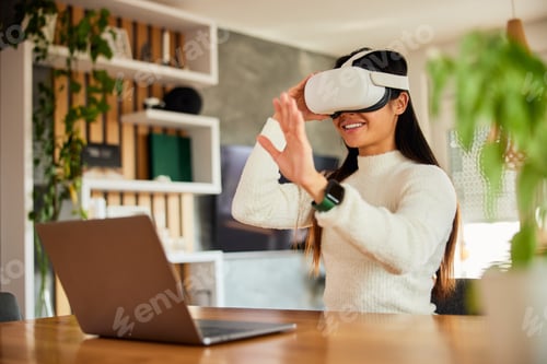 Preview: A woman testing new VR software wearing a VR headset, sitting at the workplace with a laptop.