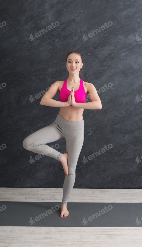 Preview: Fitness, Woman Training Yoga In Tree Pose In Gym At Grey Background, Copy Space. Young Slim Girl