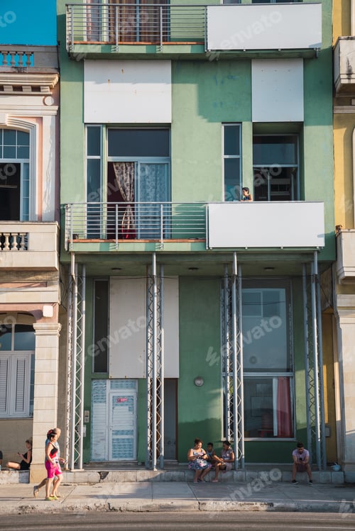 Preview: LA HABANA, CUBA - NOVEMBER, 6 , 2018: Woman on balcony of green building and street with people