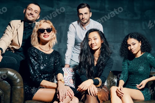 Preview: Diverse group of young beautiful people posing sitting at sofa, relax and enjoy party