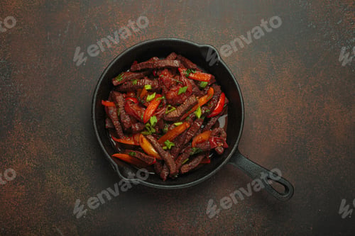 Preview: Lomo saltado, beef and red pepper stir fry cooking in cast iron pan, traditional Peruvian dish