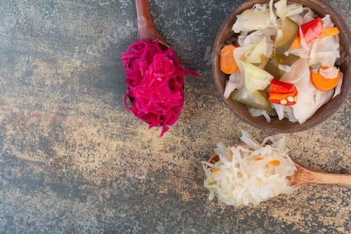 Preview: Two spoons of cabbage with wooden bowl of salty vegetables