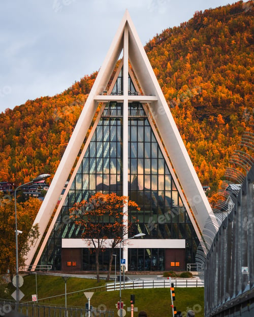 Preview: Vertical shot of the Arctic Cathedral in Tromso, Norway with autumn trees in the background