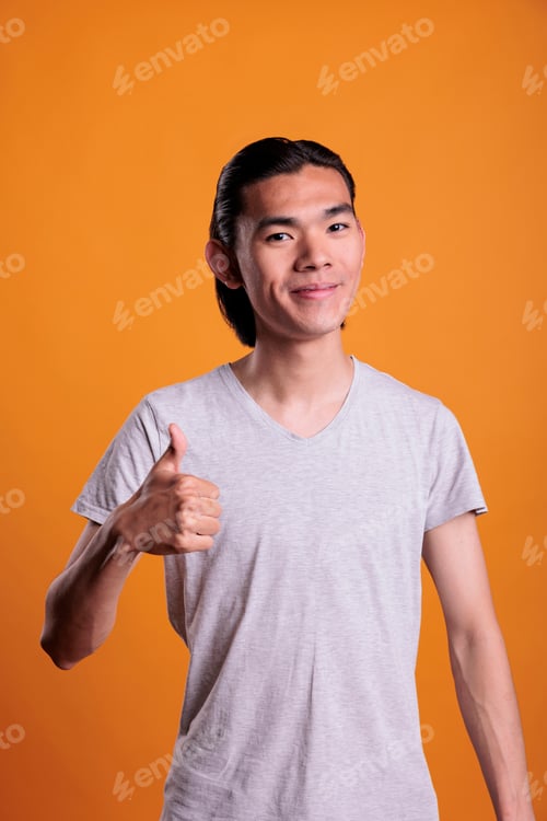 Preview: Young cheerful smiling asian man giving thumb up
