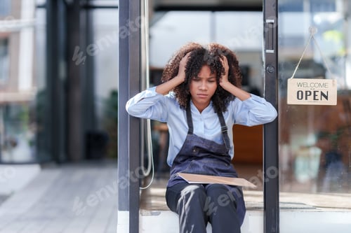 Preview: Female shopkeeper sitting stressed out at the store entrance frustrated by the economic impact.