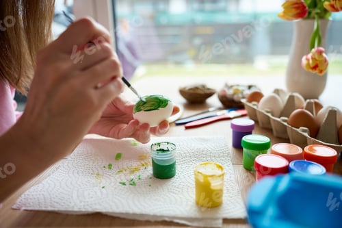 Preview: Woman painting Easter egg with green paint and brush