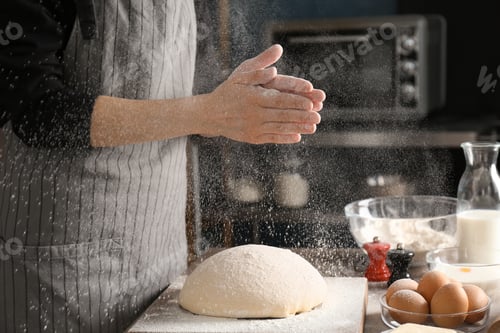 Preview: Woman sprinkling flour over dough on table in kitchen