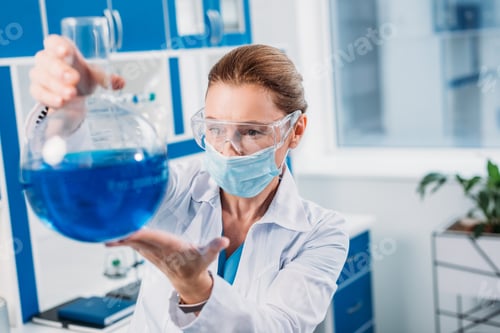 Preview: selective focus of female scientist looking at flask in hands in lab