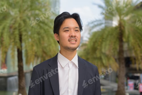 Preview: Portrait of happy Asian businessman thinking outdoors in the city