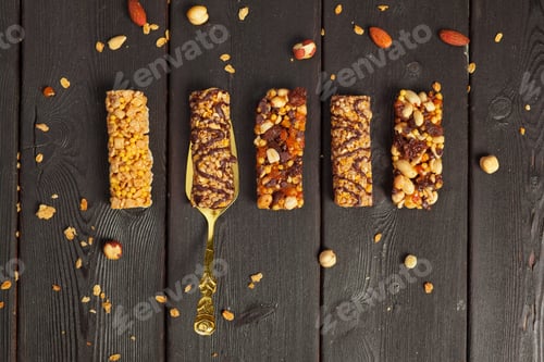 Preview: Healthy snack bars arranged on a dark wooden surface with scattered nuts nearby