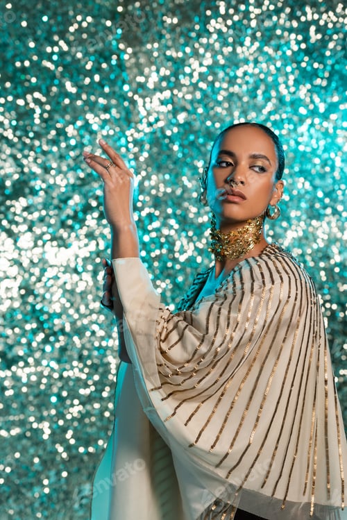 Preview: pierced african american model with gold foil on neck posing and looking away on shiny blue
