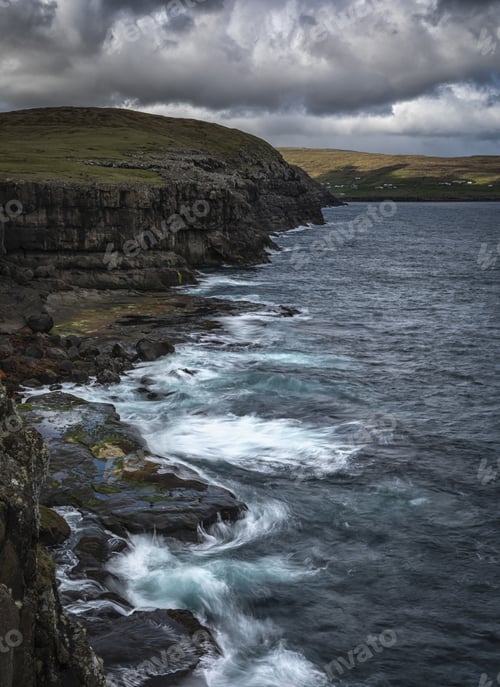 Preview: Vertical shot of sea waves hitting the shore under a blue cloudy sky