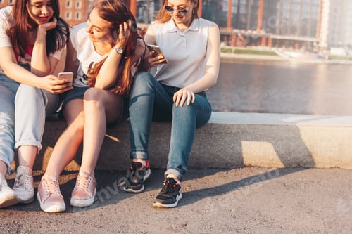 Preview: Three young happy girls real friends students using mobile at the city street on sunset background