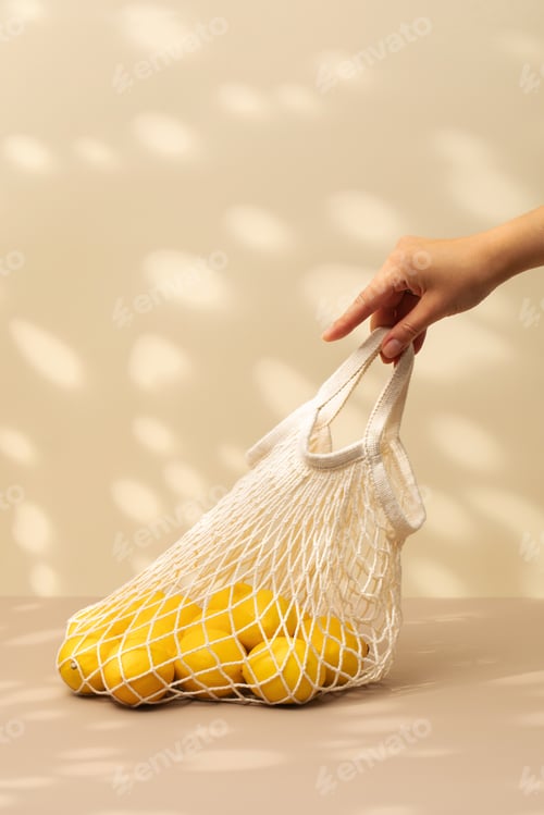 Preview: A woman's hand holds a cotton bag with yellow ripe lemons on a beige background