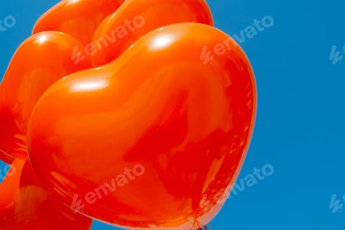 Preview: Orange heart-shaped balloons against a bright blue sky