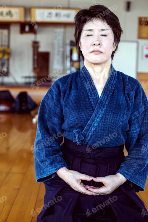 Preview: Female Japanese Kendo fighter kneeling on wooden floor, meditating.