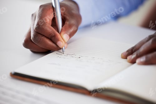 Preview: Closeup of one african american businessman writing notes in a book while working in at a desk in a