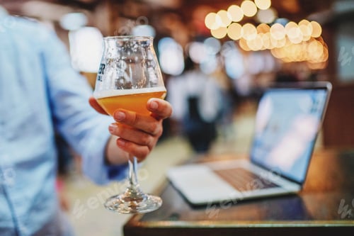 Preview: Businessman checking emails web content on laptop in natural light at cafe with a glass of beer