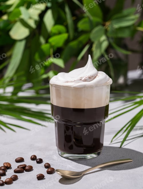 Preview: Iced coffee in a glass with foam on a light background with coffee beans and morning shadows