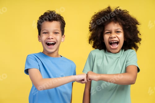 Preview: Portrait of two positive kids giving fist bump each other while screaming, posing in studio