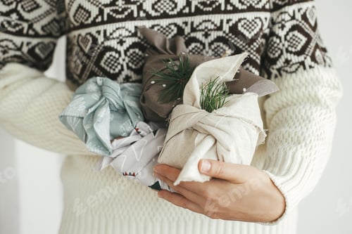 Preview: Zero waste presents, Christmas Furoshiki gifts. Woman hands in cozy sweater holding wrapped gifts