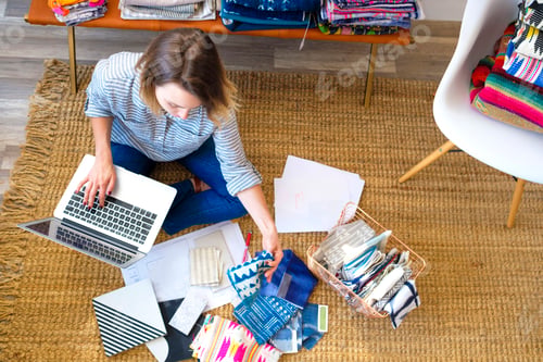 Preview: Overhead view of female interior designer using laptop on floor in retail studio