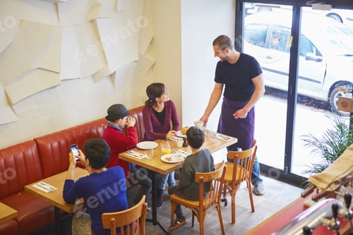 Preview: Waiter serving lunch in restaurant to family with boys
