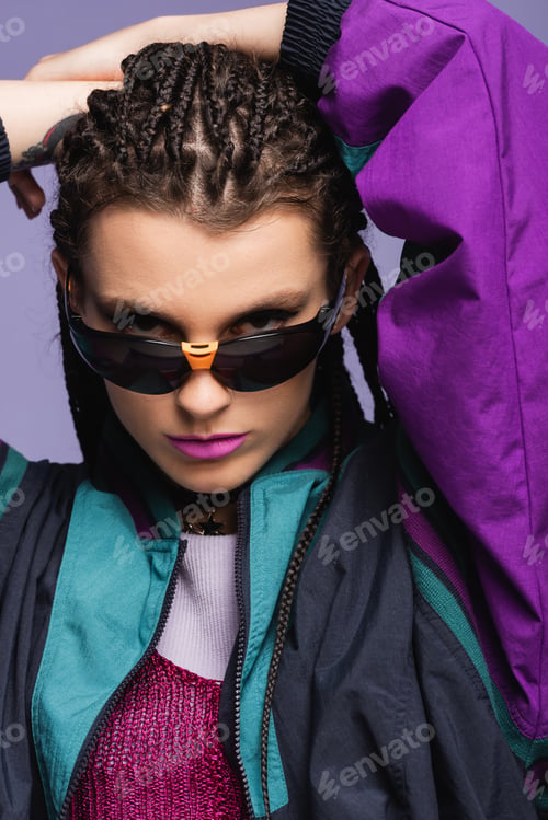 Preview: Portrait of stylish young model in retro sunglasses looking at camera isolated on purple