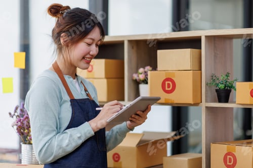 Preview: Startup SME small business entrepreneur of freelance Asian woman wearing apron using laptop and box