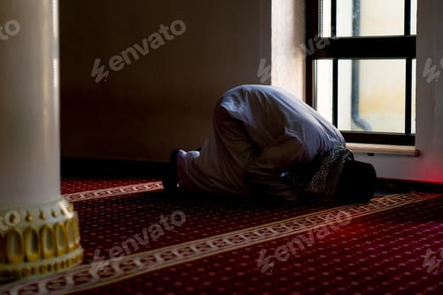Preview: A Muslim believer in national clothes prays in the twilight by the window in the mosque