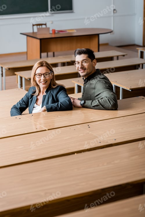 Preview: male student and female teacher looking at camera, smiling and sitting in classroom