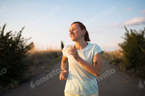Preview: Young sporty woman running on a country road at sunset