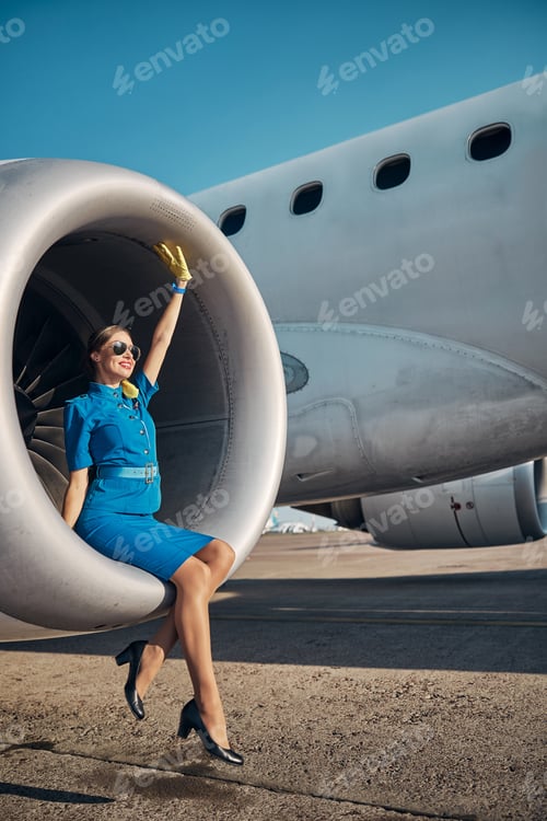 Preview: Happy stewardess relaxing on jet turbine outdoors
