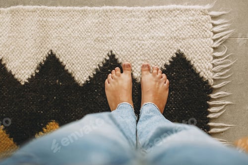 Preview: Feet on cozy woolen rug on background of concrete floor. Woman barefoot standing on modern rug