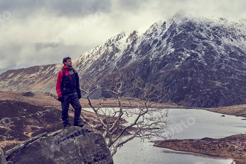 Preview: Male hiker looking out at lake and snow capped mountain landscape, Llanberis, Gwynedd, Wales