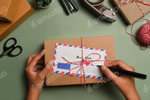 Preview: From above view of woman signing greeting card, surrounded by gift wrapping materials.