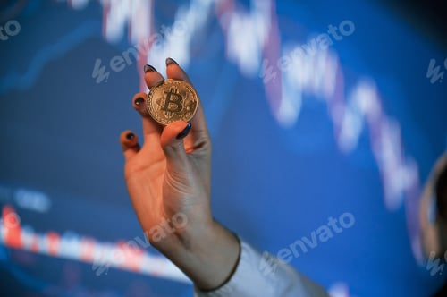 Preview: Close up view of woman's hand that holding physical bitcoin against background with graphs