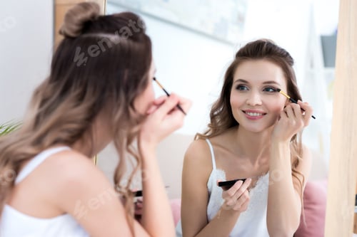 Preview: beautiful smiling girl looking at mirror and applying makeup
